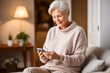 Elderly woman who adapts to new technologies, connects and communicates, using a smartphone sitting on the sofa at home