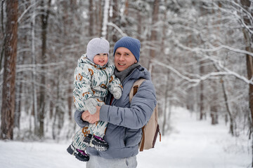 Wall Mural - A young father and a littl child of 2 years old are laughing and having fun in a snowy winter forest on a walk