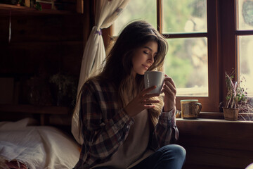 young woman drinking coffee while sitting near the window in the hom