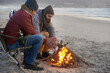 © AW/peopleimages.com - Campfire, friends and adventure with men by the beach at sunset with vacation and camping. Ocean, outdoor and together with travel and people in a trip and journey with fire and conversation by sea