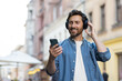 © Tetiana - Bearded mature man enjoying music on headphones while using smartphone in city