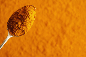 Wall Mural - Turmeric root powder on a spoon on orange background with copy space