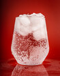 A glass of refreshing sparkling mineral water with ice on a red background
