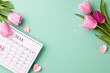 May's blossoming gratitude: honoring motherhood. Top view shot of vibrant tulips surrounding a calendar on a refreshing turquoise background with space for loving messages