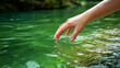 © Vitor - Mão de uma mulher segurando uma gota de água em um fundo de água verde