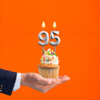 The hand that delivers cupcake with the number 95 candle - Birthday on orange background