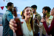 © CarlosBarquero - Portrait attractive young blonde smiling woman showing blurred beer bottle on camera. Pretty generation z girl posing joyful for photo at party friends outdoor at sunset. People celebrating on rooftop