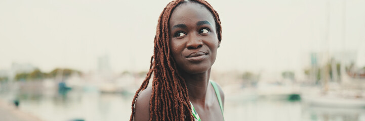 Wall Mural - Woman with African braids wearing top looks at the yachts and ships standing on the pier in the port, Panorama.