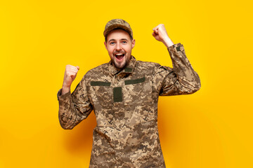 Wall Mural - Ukrainian army soldier in pixel camouflage uniform celebrates victory and success on a yellow isolated background, Ukrainian military cadet winner rejoices in good luck
