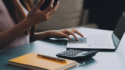 Wall Mural - Woman hand holding white mobile phone on a table with a laptop in office.