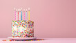 © wanchai - Birthday celebration cake with burning candles and colorful confetti on a soft pink background.