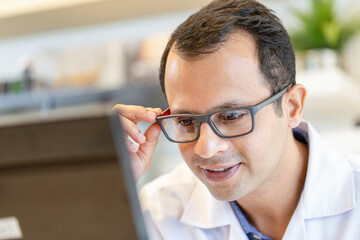 Wall Mural - Cheerful optometrist man holding eyeglasses in optics store, Indian man choosing glasses at optics shop