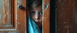 © AkuAku - Curious young boy peeking out from behind an old wooden door in a spooky abandoned house
