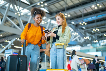 Happy woman friends holding passport and luggage walking together to airline check in counter in airport terminal. Attractive girl enjoy and fun travel on holiday vacation with airplane transportation