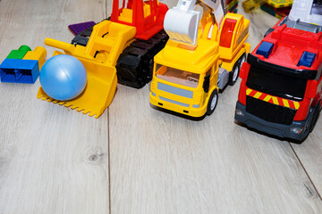 Wall Mural - children's toy cars made of plastic, a fire truck, an excavator, a tractor, are on the floor.