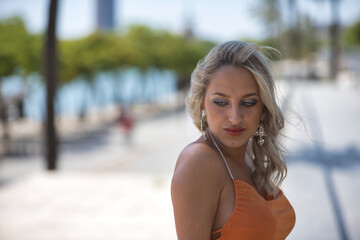 Wall Mural - Portrait of beautiful young woman, blonde with blue eyes and an orange dress, leaning on a railing looking at the ground with melancholy and sadness. Concept beauty, fashion, sorrow, melancholic.