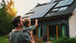 Father carrying son outdoors and pointing on solar panel on the roof