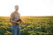 © Serhii - Agronomist inspecting soya bean crops growing in the farm field. Agriculture production concept. young agronomist examines soybean crop on field in summer. Farmer on soybean field