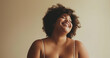 Studio portrait of youthful curvy black girl in camisole laughing, brown short hair, beige background