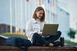 Conception of learning, sitting with laptop. Young female student in casual clothes is outdoors