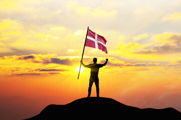 Denmark flag being waved by a man celebrating success at the top of a mountain against sunset or sunrise. Denmark flag for Independence Day.