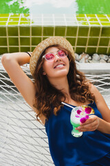 Wall Mural - attractive young woman in blue dress and straw hat wearing pink sunglasses drinking cocktails