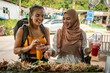 © Connect Images - Two young women one wearing a hijab laughing together buying street food.