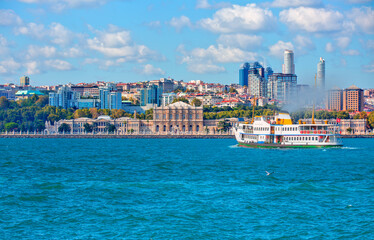 Wall Mural - Sea voyage with old ferry (steamboat) in the Bosporus - Dolmabahce Palace  seen from the Bosphorus - Dolmabahce palace against coastal cityscape with modern buildings under cloudy sky - istanbul