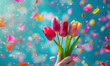 vibrant tulips bouquet held by a female hand celebration with colorful confetti on turquoise background, women's and mother's day concept 
