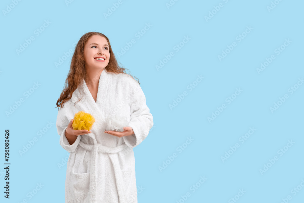 Young woman in bathrobe with loofahs on blue background