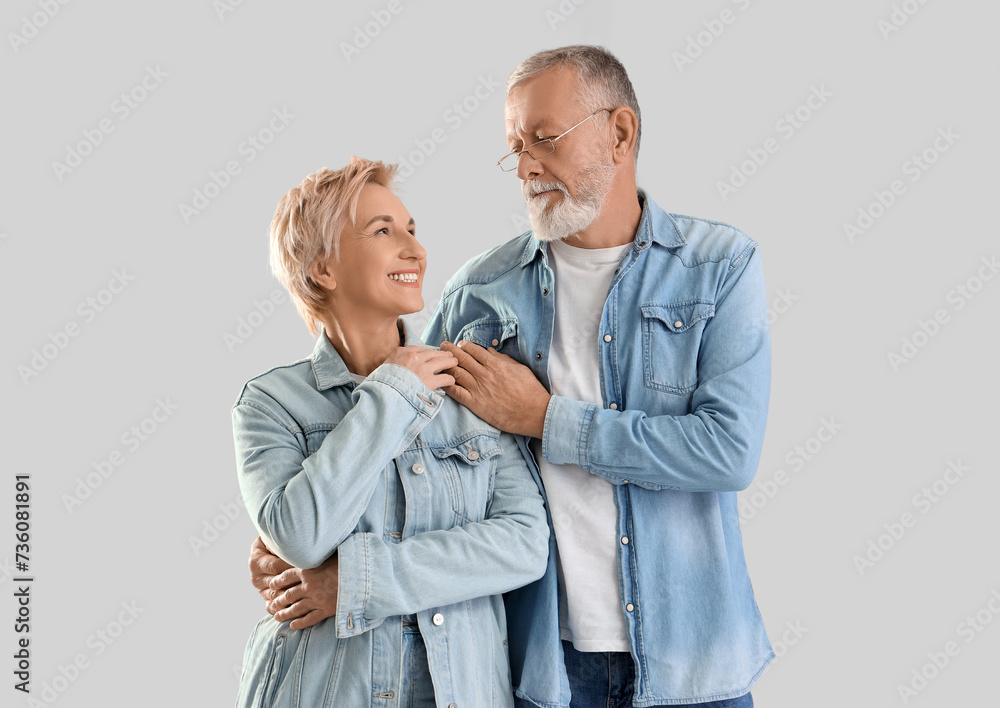 Mature couple in denim jackets hugging on light background
