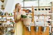 © nataliaderiabina - Smiling woman buying organic food and eco products in sustainable plastic free store. Happy female customer shopping at local grocery shop.