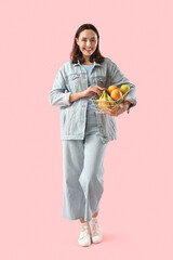 Wall Mural - Young woman with basket of fruits on pink background