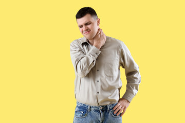 Wall Mural - Young man suffering from neck pain on yellow background