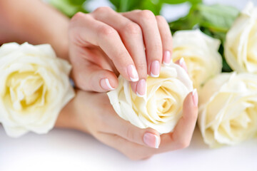 Wall Mural - Hands of a woman with beautiful french manicure and white roses