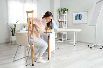 Sticker - Injured young woman after accident with crutches standing up from chair in clinic