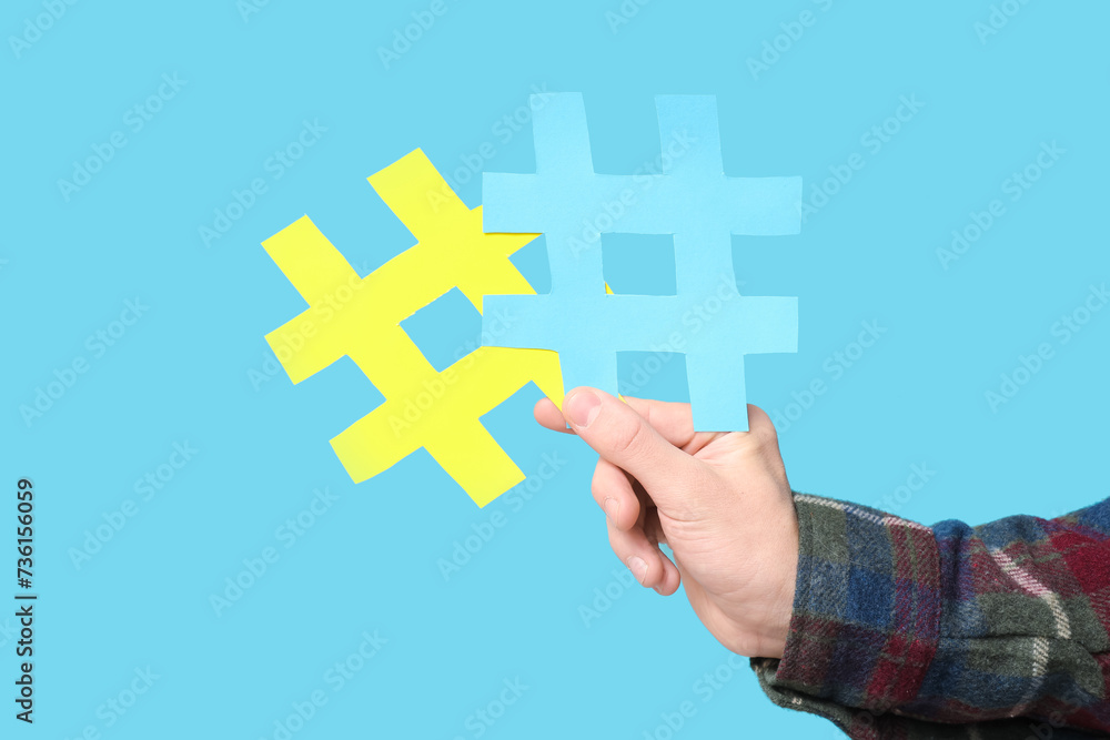 Hand of young man with hashtag symbols on blue background