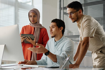 Poster - Team of three young Muslim employees looking at computer screen while confident man explaining online data to his colleagues