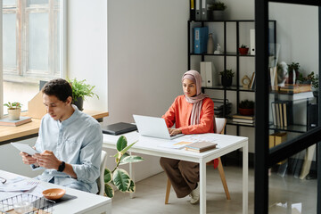 Leinwandbilder - Young Muslim businesswoman in hijab sitting by workplace in coworking space and looking at laptop screen while analyzing data