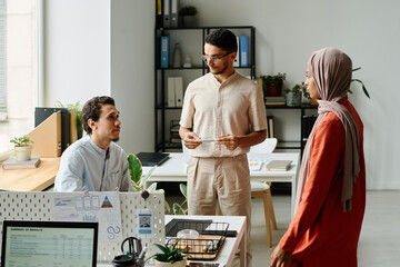 Leinwandbilder - Group of three young intercultural Muslim business people discussing points of new project at start-up meeting in coworking space
