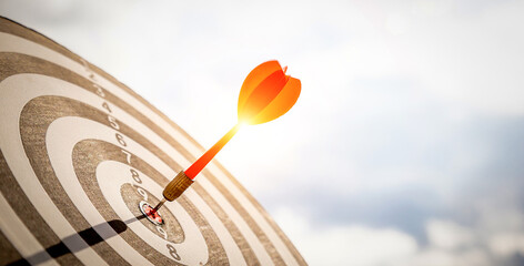 Close up shot red darts arrows in the target  of dartboard center on dark blue sky background. Business target or goal success and winner concept.