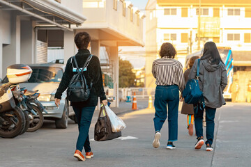 Back view of Asian elderly woman traveler in casual clothes walks down a street with travel bag in morning. Senior woman tourist walks with her travel bag. Vacation and travel elderly people concept.