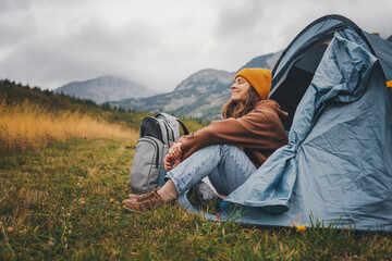 Wall Mural - Young woman enjoying landscape sitting in the tent alone, engoy nature and relax. Traveling and camping concept. Camping tent