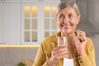 Menopause, hormone replacement therapy. Happy woman holding glass of water and pill in kitchen, space for text