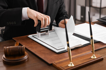 Poster - Notary stamping document at wooden table in office, closeup