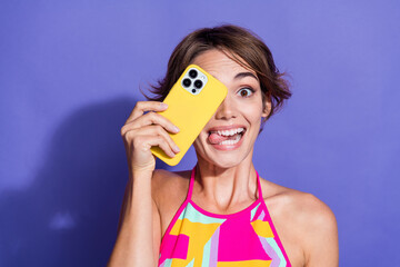 Sticker - Photo of young lady in pink singlet crazy face hide eye photographer amateur using smartphone tongue out isolated on purple color background