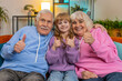 © Andrii Iemelianenko - Like. Happy excited Caucasian grandparents and granddaughter looking at camera and showing thumbs up sign positive great news positive feedback. Cheerful family sitting on sofa in living room at home.