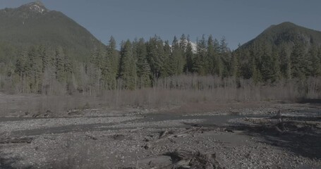 Wall Mural - Ungraded 4k low altitude wide-angle drone footage flying above a river in a valley surrounded by mountains and forest on a sunny winter morning in Washington State.