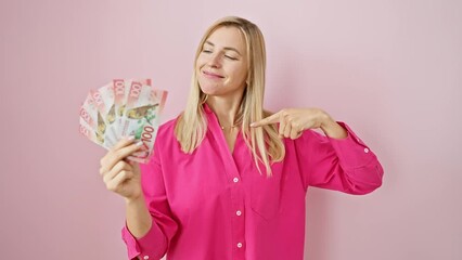 Sticker - Cheerful young blonde woman proudly displaying new zealand dollars, pointing with optimistic smile, over isolated pink background