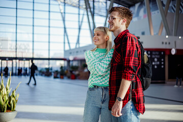 Wall Mural - Young passengers hugging and looking at something at train station.